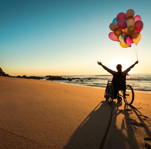 Disabled woman in a wheelchair holding balloons on the beach
